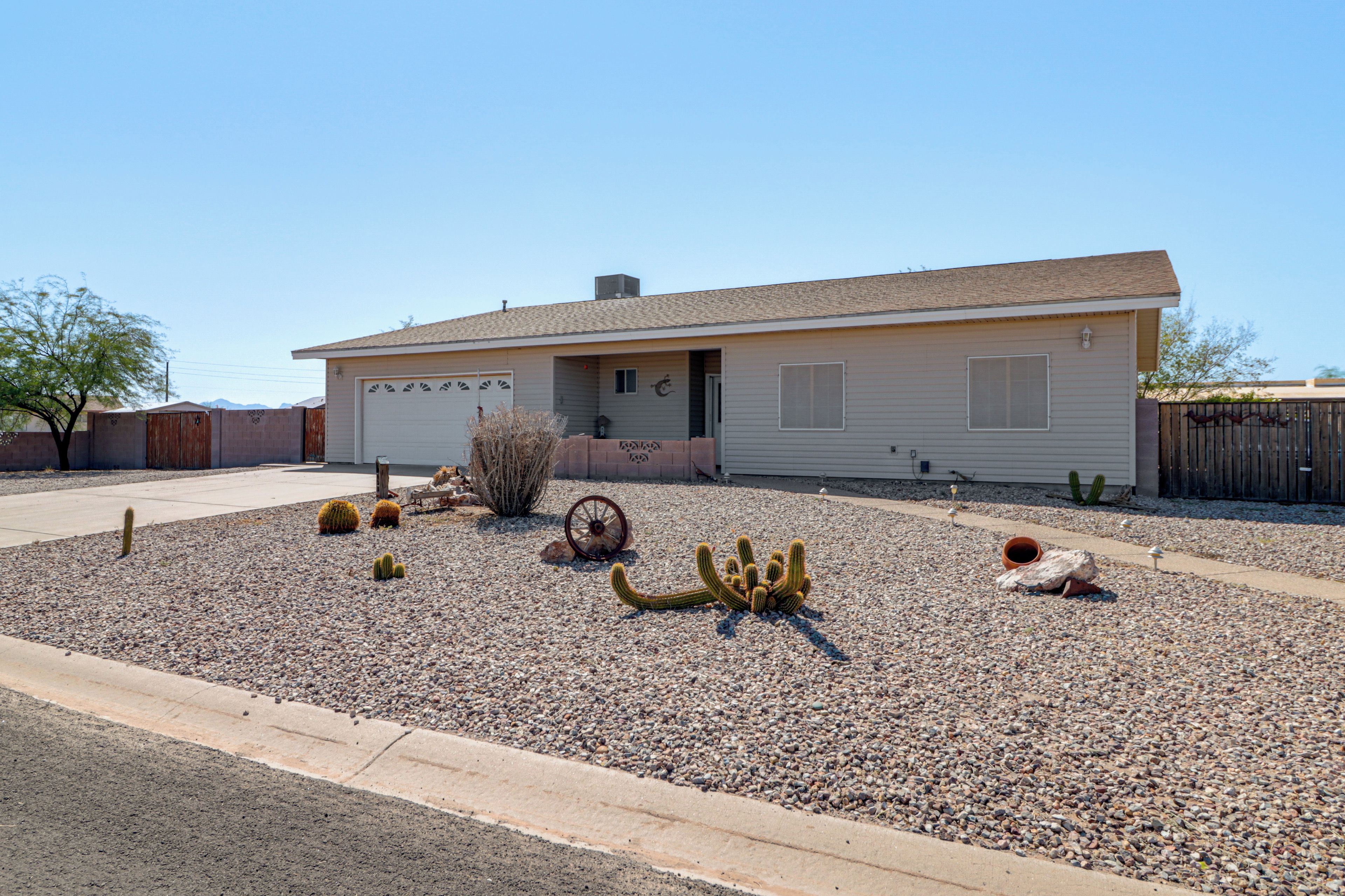A single-story house with a garage, surrounded by a gravel driveway and various cacti.