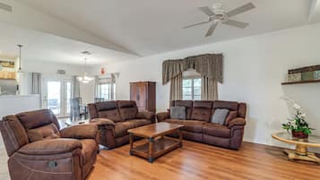 A spacious living room with a brown leather sofa set, a wooden coffee table, and a ceiling fan.