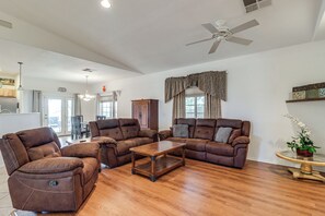 A spacious living room with a brown leather sofa set, a wooden coffee table, and a ceiling fan. - Arizona City Monthly Rental w/ Yard & Workspaces (Arizona City)