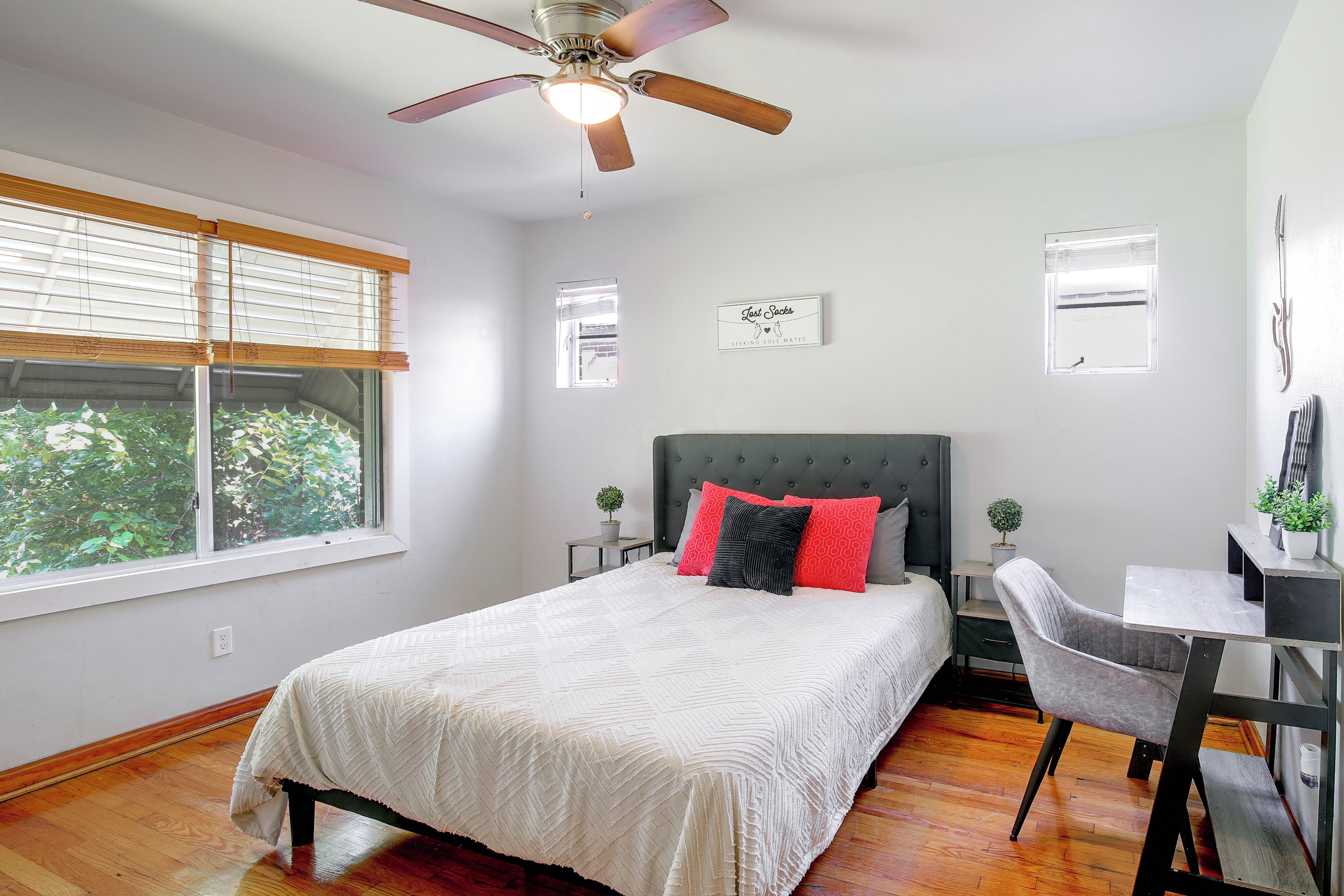 A bedroom with a bed, a desk, a chair, a ceiling fan, and a window with blinds.