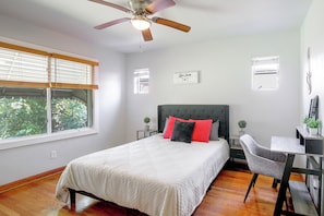 Ein Schlafzimmer mit Bett, Schreibtisch, Stuhl, Deckenventilator und einem Fenster mit Jalousien.