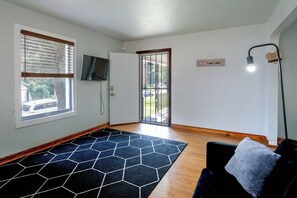 A room with a black hexagonal rug, a door leading outside, a television mounted on the wall, and a light fixture.
