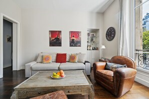 Ein Wohnzimmer mit einem grauen Sofa, einem braunen Ledersessel, einem Couchtisch mit Obst und Kunstwerken an der Wand.
