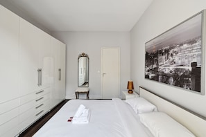 Ein modernes Hotelzimmer mit einem großen Bett, einem Kleiderschrank, einem Schminktisch mit Spiegel und einem Stadtbild an der Wand.