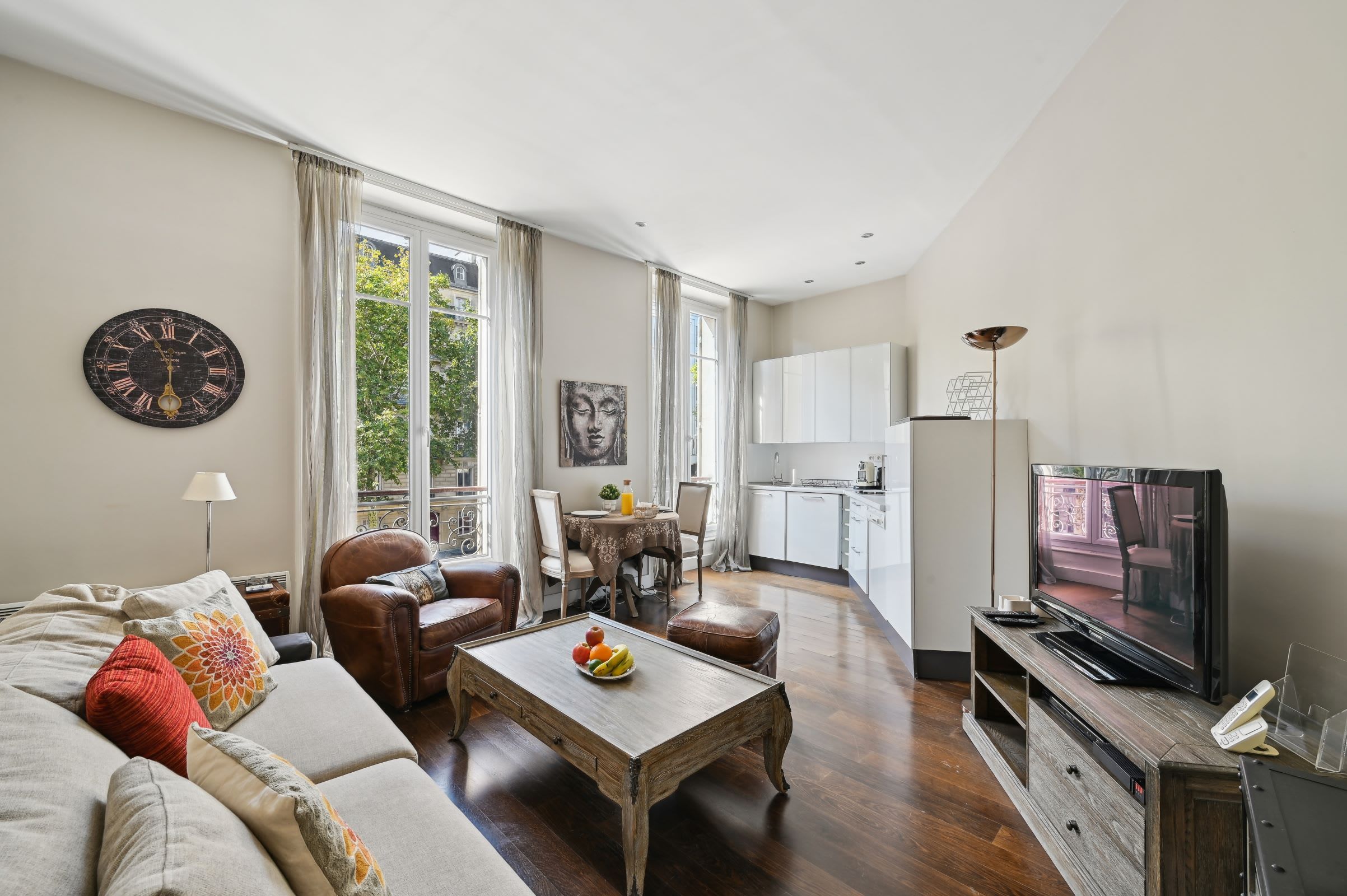Ein modernes Wohnzimmer mit Sofa, Couchtisch und Fernseher. Es gibt eine Essecke mit Tisch und Stühlen sowie eine Küche im Hintergrund.