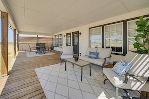Un'area patio coperta con un pavimento in legno, mobili da esterno e ampie finestre.