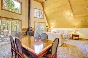 A spacious living area with a high ceiling, a dining table with chairs, a sofa, and a fireplace. - Calaveras Adventure Lodge in Blue Lake Springs (Arnold)