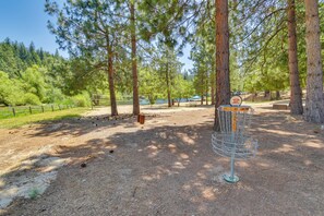 A disc golf course with a metal basket, surrounded by tall pine trees and a dirt path. - Calaveras Adventure Lodge in Blue Lake Springs (Arnold)