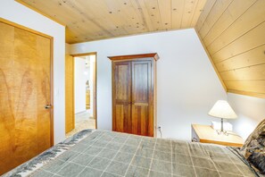 A bedroom with a wooden ceiling, a door, a bedside table with a lamp, and a bed with a patterned blanket. - Calaveras Adventure Lodge in Blue Lake Springs (Arnold)