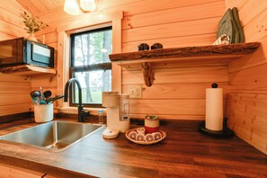 Une cuisine avec des murs en bois, un évier en acier inoxydable, un four à micro-ondes, une machine à café et une fenêtre donnant sur les arbres.