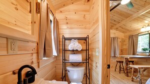Ein Holzblock-Interieur mit Bad, inklusive Waschbecken, Toilette, Handtuchhalter und einem Fenster mit Vorhängen.