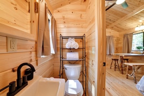 A wooden cabin interior with a bathroom, a sink, a toilet, a towel rack, and a window with curtains. - Cozy Couple’s Cabin w/ Trail Access in Oxford (Oxford)