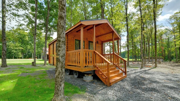 Eine Holzhütte mit Veranda und Stufen, umgeben von Bäumen und Kiesgrund.
