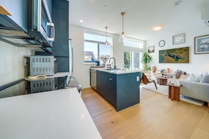 A modern kitchen with a central island, built-in appliances, and a dining area with a sofa and coffee table. - Rooftop Fire Pit & Mtn Views! Seattle Townhome (Seattle)