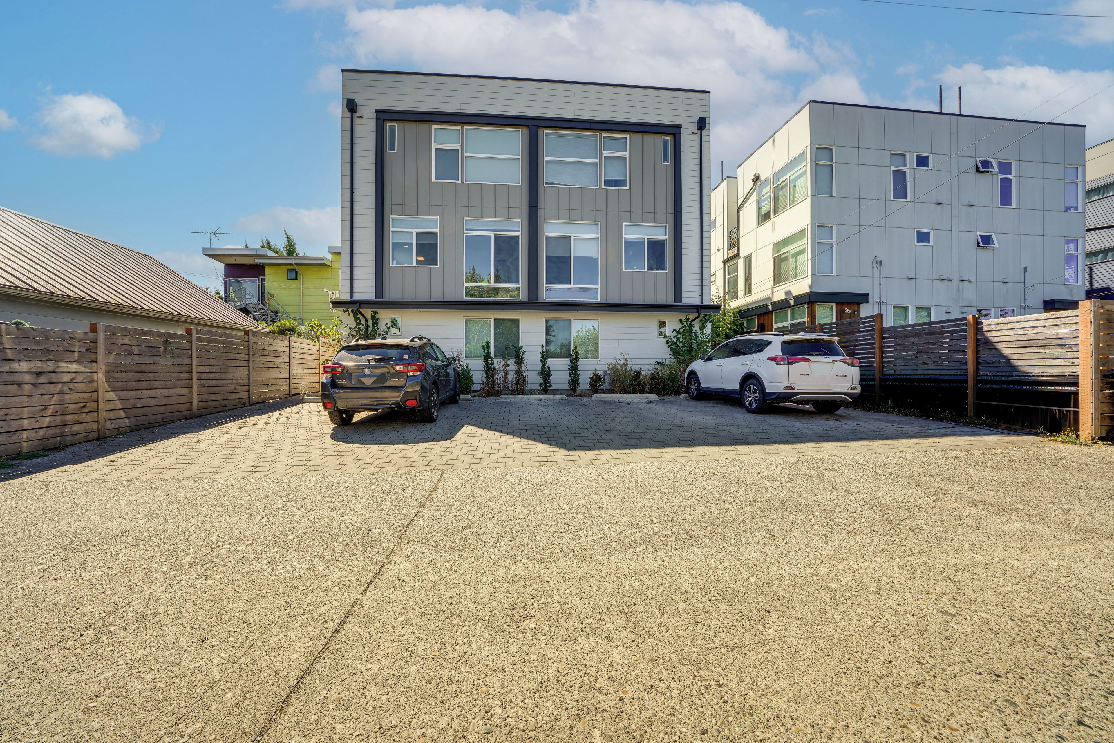 A modern two-story building with a flat roof, large windows, and a paved driveway.