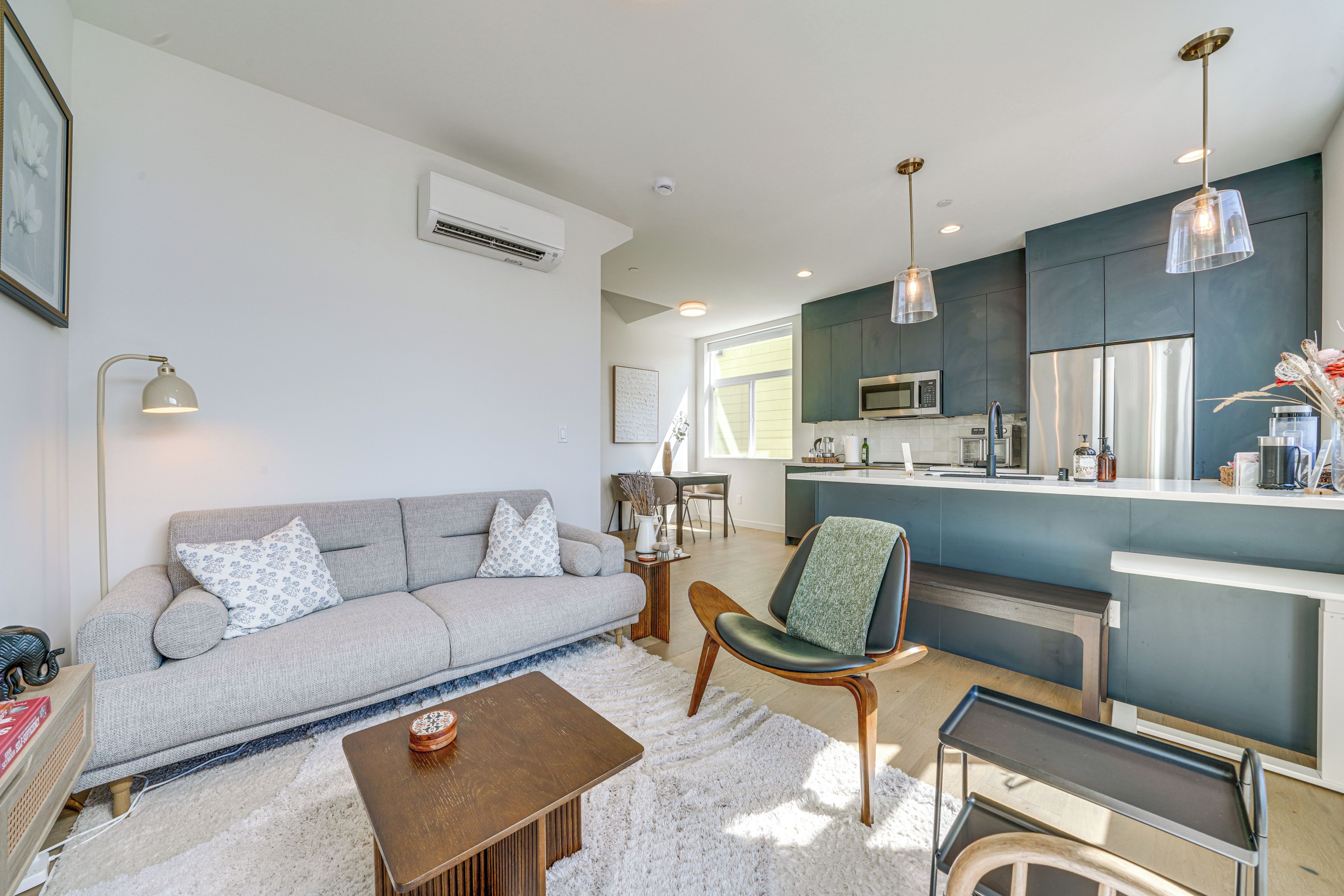 A modern living room with a grey sofa, a wooden coffee table, and a kitchen area with a blue accent wall, a microwave, and a refrigerator.