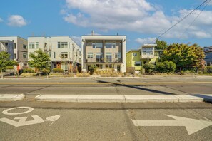 A street view with modern multi-story residential buildings, a clear sky, and a bicycle lane. - Rooftop Fire Pit & Mtn Views! Seattle Townhome (Seattle)