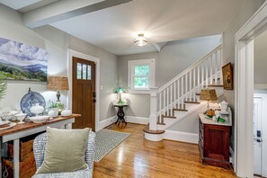 A well-lit hallway with a wooden staircase, a dining area with a table and chairs, and a painting on the wall. - Downtown Salem Home: Walk to Main Street! (Salem)