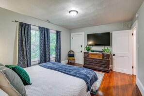 Quarto com cama, cômoda, televisão e janela com cortinas.