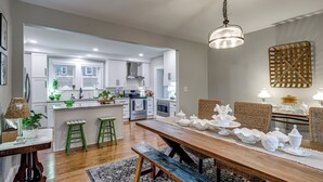 A modern kitchen with white cabinetry, a dining area with a wooden bench, and a hanging light fixture. - Downtown Salem Home: Walk to Main Street! (Salem)