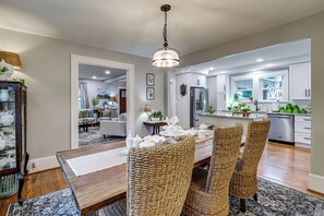 A modern kitchen with white cabinets, a stainless steel refrigerator, and a dining area with wicker chairs and a wooden table. - Downtown Salem Home: Walk to Main Street! (Salem)