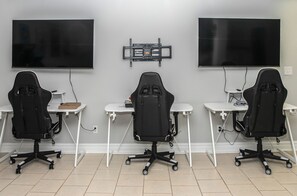 A room with three gaming chairs, two desks, and two large flat-screen TVs mounted on the wall. - Waterfront Deck, Family Arcade! Lake Gaston Home (Bracey)
