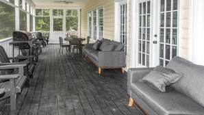 Eine überdachte Veranda mit Grill, Sitzgelegenheit und großen Fenstern.
