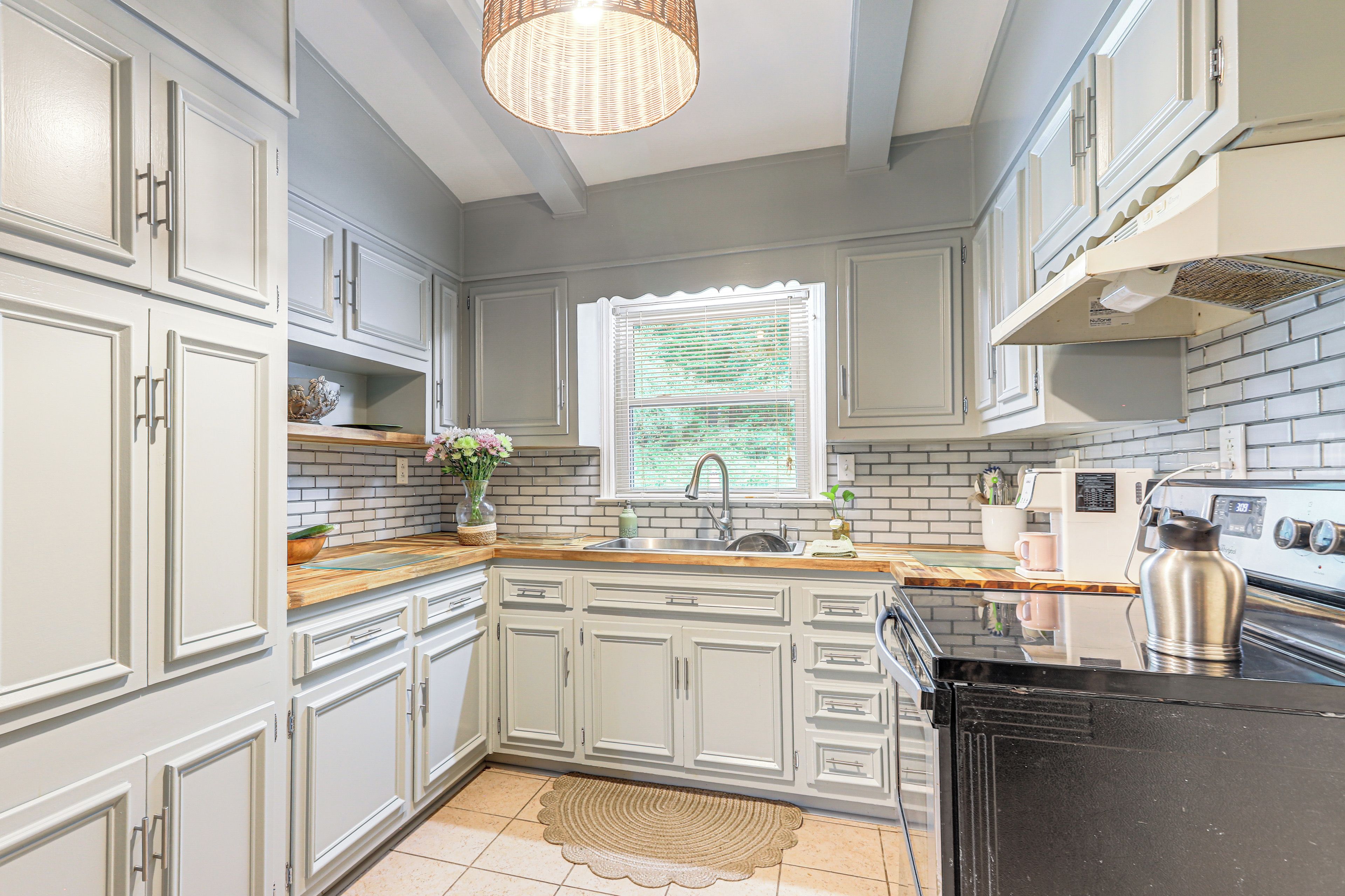 A kitchen with grey cabinets, a wooden countertop, a sink, and a stove.