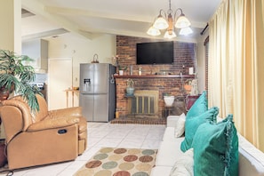 A living room with a sofa, a coffee table, and a television mounted on a brick wall. There is a kitchen area with a refrigerator and a microwave. - Cozy Georgia Gem on 3.5 Acres: Eat, Shop, Explore! (Fayetteville)