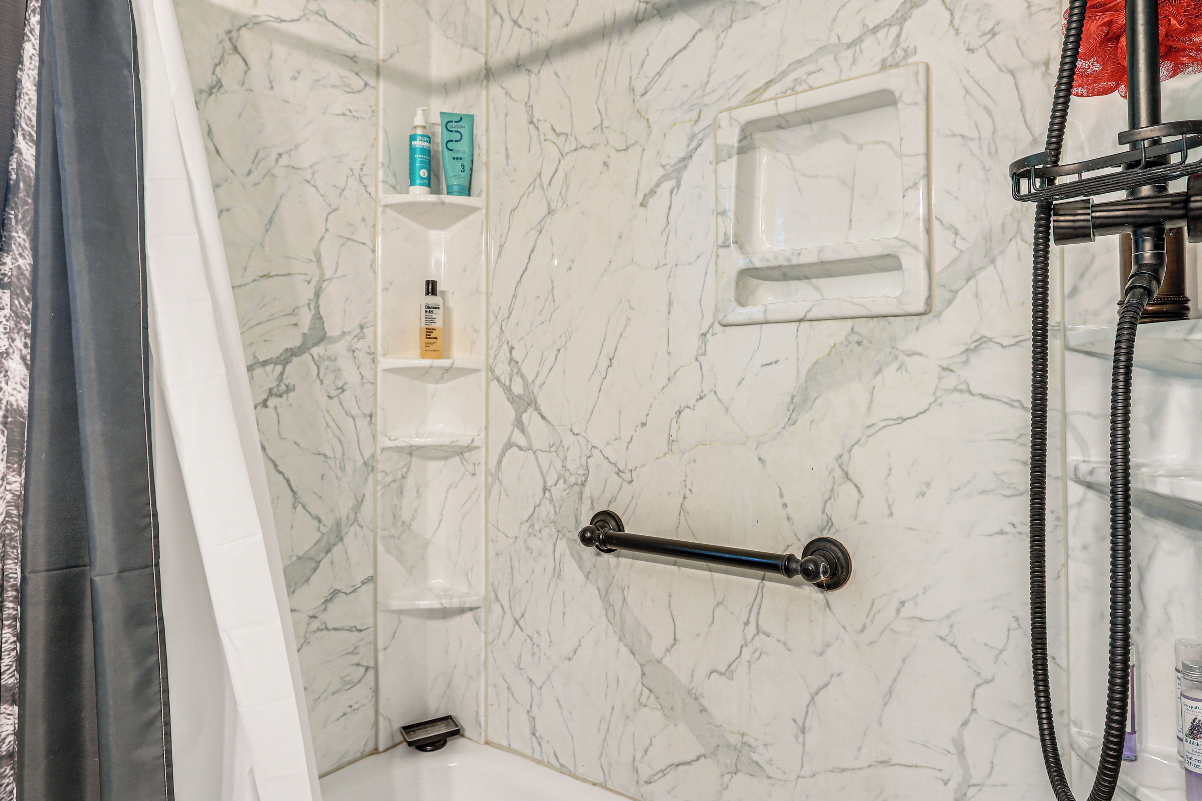Un bagno con parete in marmo, zona doccia e un ripiano con articoli da toilette.