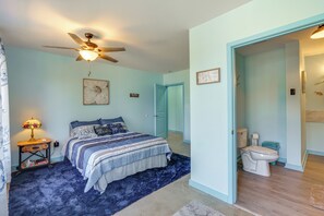 Een slaapkamer met een bed, een plafondventilator, een nachtkastje, een lamp, en een badkamer met toilet en douche.