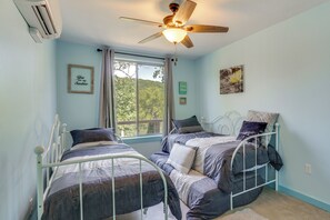 Une chambre avec deux lits superposés en métal, un ventilateur de plafond, une fenêtre avec des rideaux et des décorations murales.