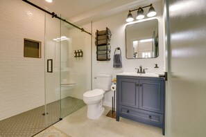 Un bany modern amb un pavelló de dutxa de vidre, un vàter blanc, un lavabo blau amb un mirall i un suport de tovalloles amb tovalloles doblegades.