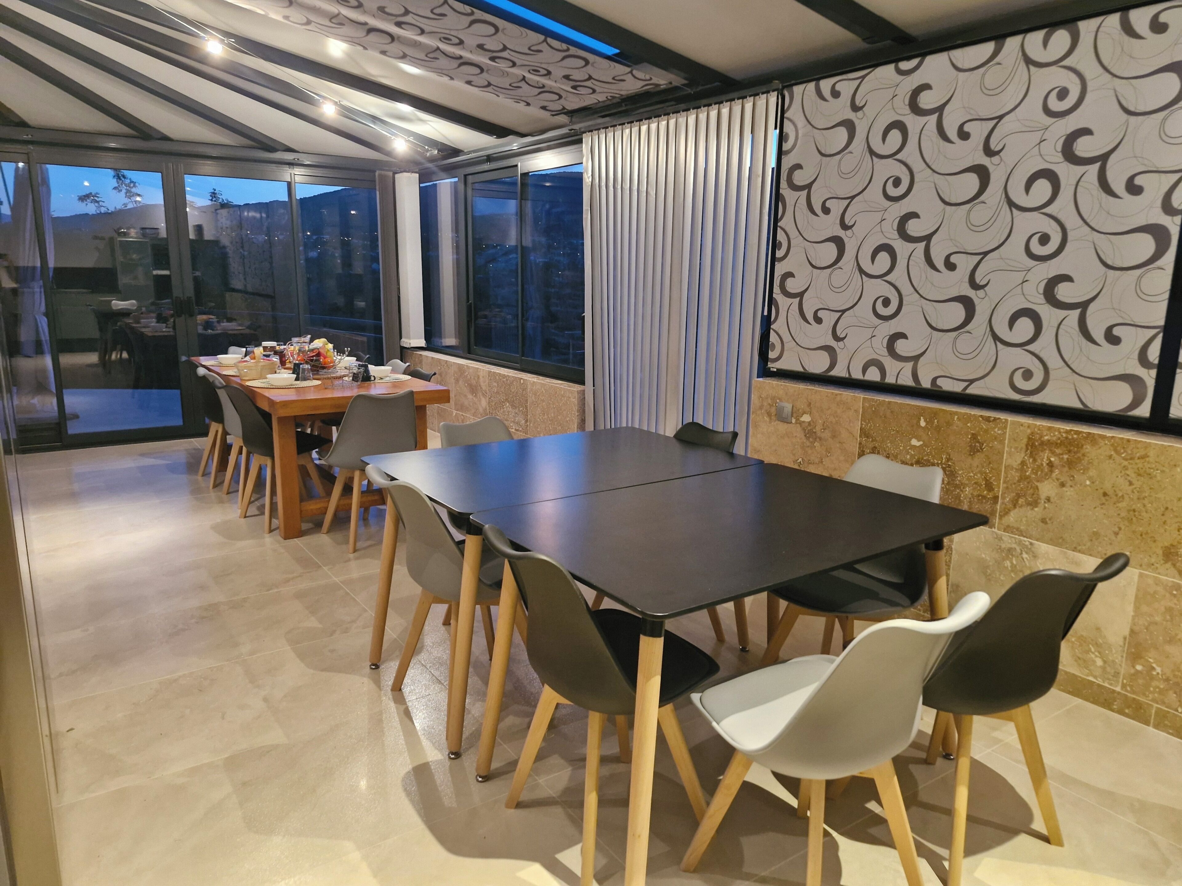 Een moderne eetruimte met een grote tafel en stoelen, een patroonmuur en een uitzicht door grote ramen.
