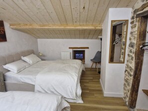 Une chambre avec un plafond en bois, un lit avec une literie blanche, une chaise et un téléviseur.
