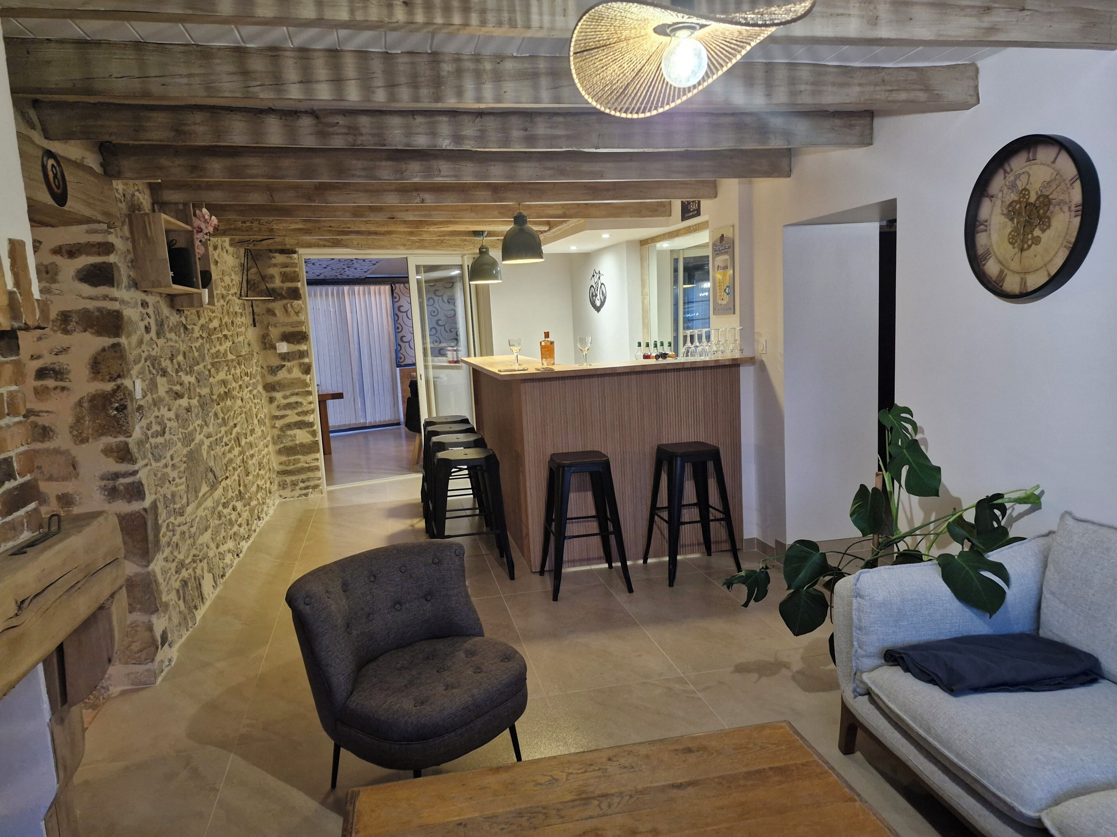 Un espace de vie chaleureux avec un mur en pierre, un bar avec des tabourets, un canapé et une plante en pot.