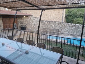 Une table avec un plateau en verre, des chaises, une piscine et un mur de pierres en arrière-plan.