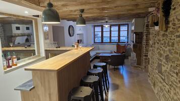 A rustic kitchen with a wooden bar and stools, a stone wall, and a large window with a view.