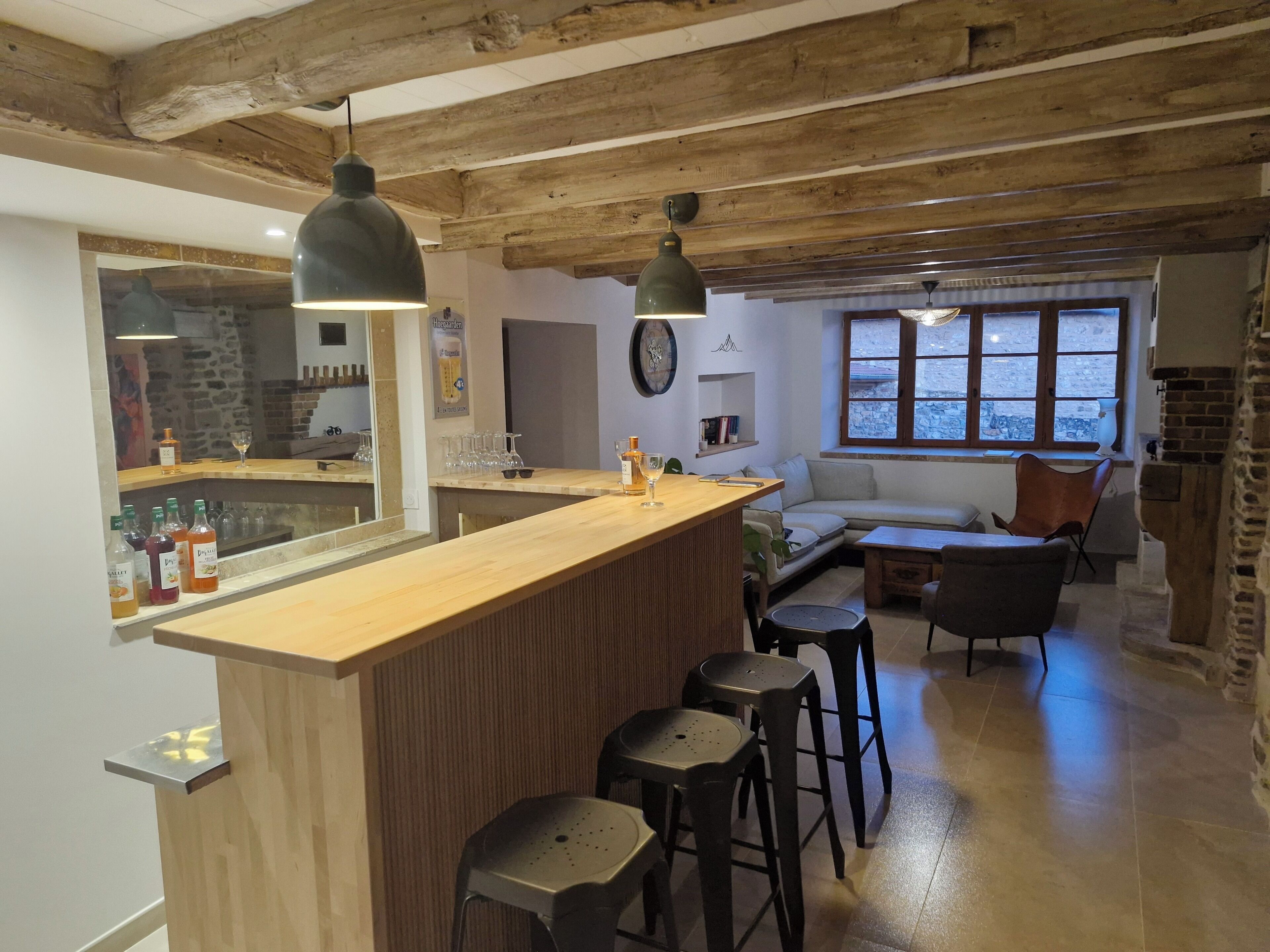 A rustic interior with a wooden bar, stools, a sofa, and a large window.
