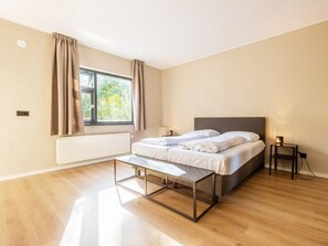 Ein modernes Schlafzimmer mit einem Bett, Nachttischen, einer Bank und einem Fenster mit Vorhängen.