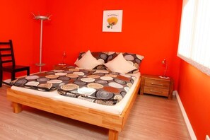 Een kamer met een bed, een stoel, een nachtkastje, een vloerlamp en een schilderij aan de muur.
