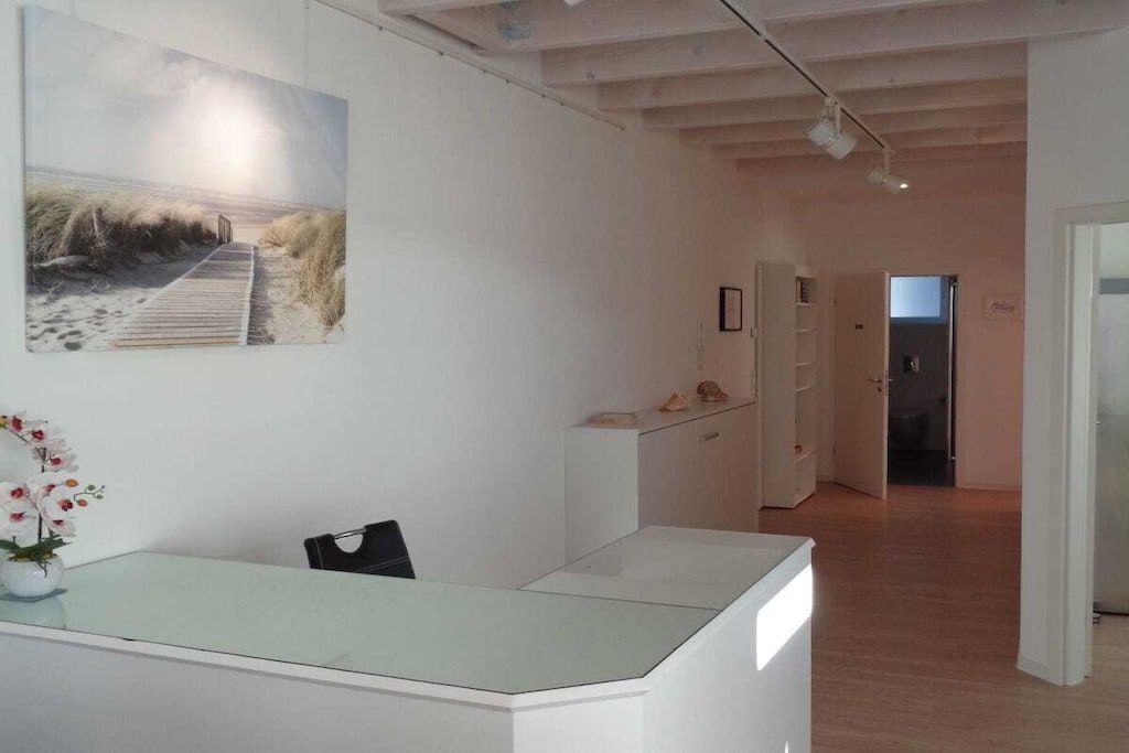 A reception area with a glass desk, a framed artwork on the wall, and a pathway leading to a door.