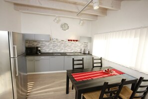 Une cuisine moderne avec des meubles gris, un réfrigérateur en acier inoxydable et un coin repas comprenant une table et des chaises en bois.
