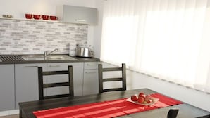 Eine moderne Küche mit grauen Schränken, einer Spüle aus Edelstahl und einem Toaster. Ein Esstisch mit einer roten Tischdecke und einer Schüssel mit Obst.