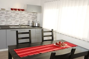 Een moderne keuken met grijze kastjes, een roestvrijstalen spoelbak en een broodrooster. Er staat een eettafel met een rode placemat en een schaal met fruit.