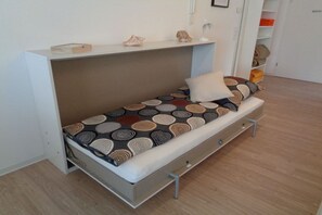 Un lit compact avec un matelas à motifs, un oreiller et une table de chevet avec une lampe.