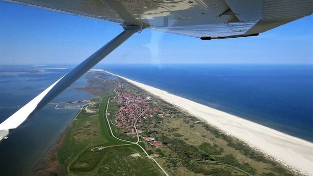 Luftaufnahme einer Küstenlandschaft mit Strand, einer Stadt und einem Gewässer.