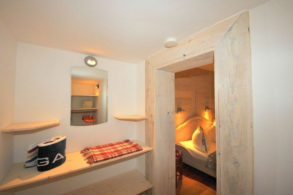 A bathroom with a wooden door, a mirror, and a shelf with towels and a roll of toilet paper.