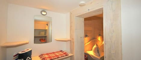A bathroom with a wooden door, a mirror, and a shelf with towels and a roll of toilet paper.