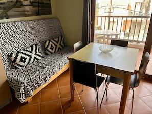 A room with a patterned sofa, a small dining table, and a view through a window. - Studio apartment in beachfront complex & 2 minutes walk to town (Santa Maria)